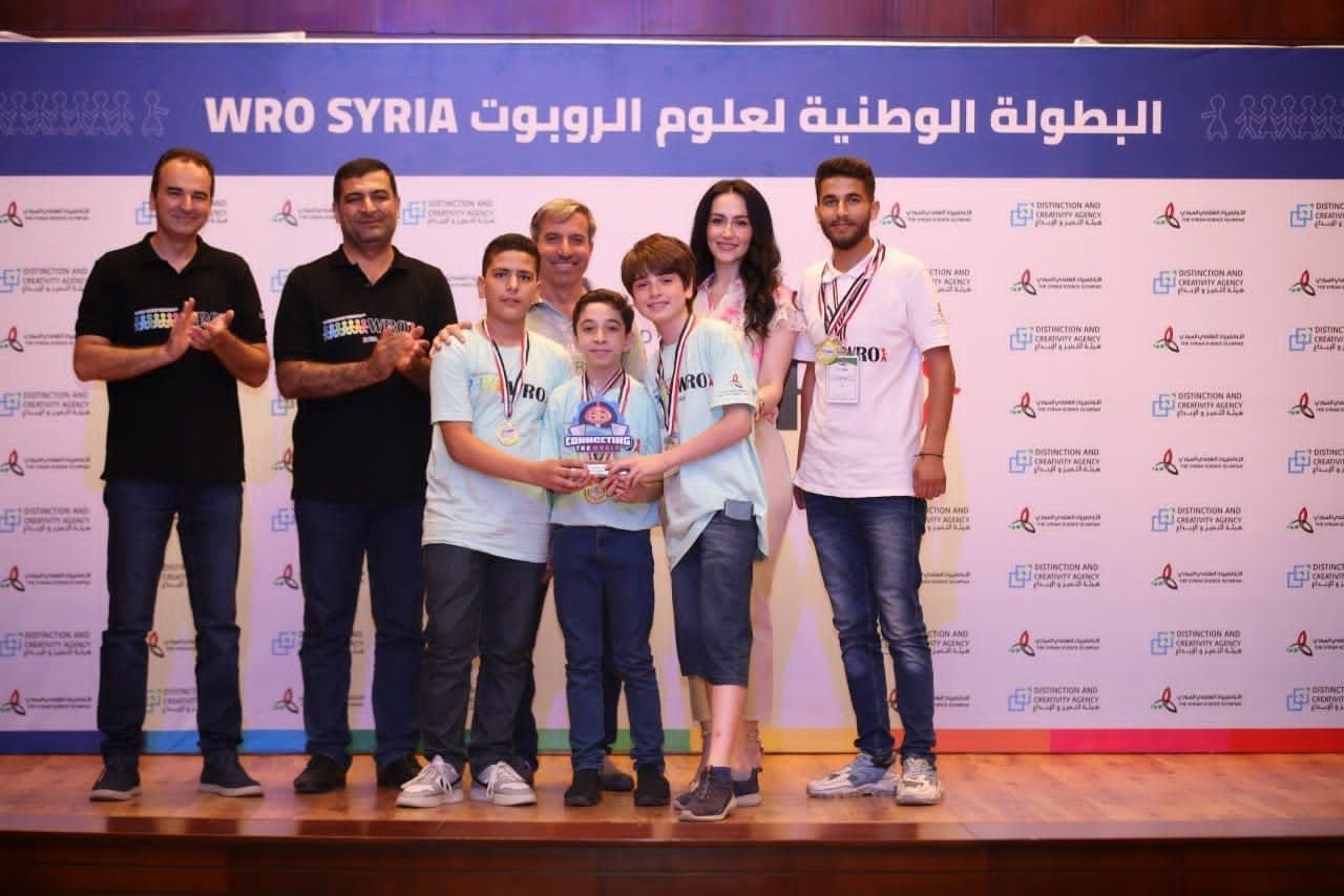 Team Astronauts with their gold medals and trophy on stage at WRO Syria 2023, with their coach Ward Alkhatib